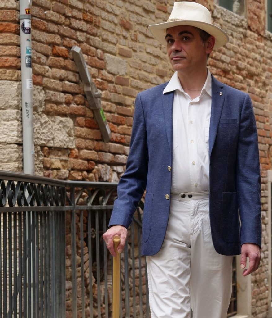 Raffaele Dessì, uomo elegante con bastone da passeggio in legno di briccola davanti a un muro veneziano